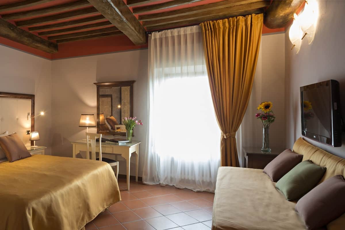 A hotel room with a large bed, a sofa, a desk with a lamp, a mirror, and a TV mounted on the wall.