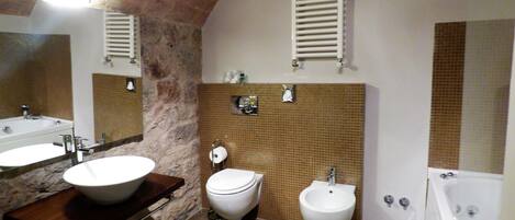 A bathroom with a stone accent wall, a large sink, a toilet, a bidet, and a bathtub.