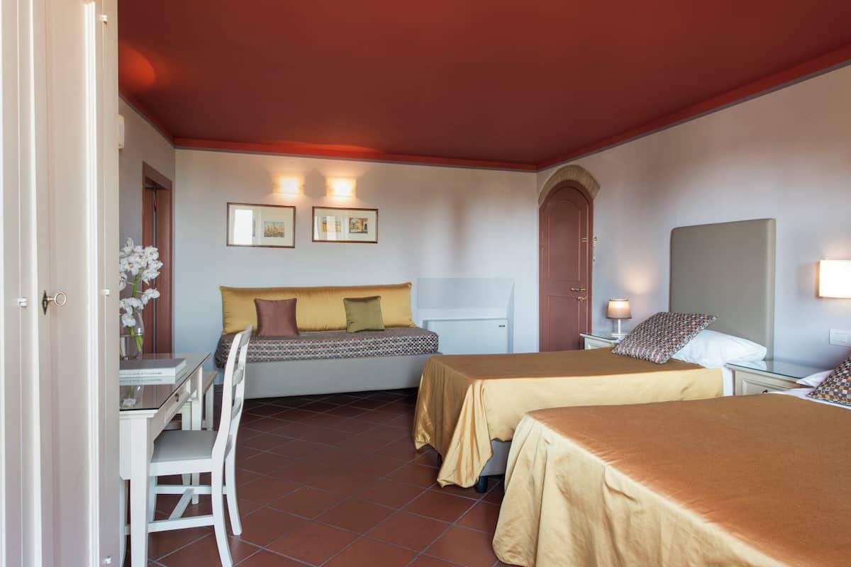 A hotel room with two beds, a desk, and a chair. There are framed pictures on the wall and a door with a handle.