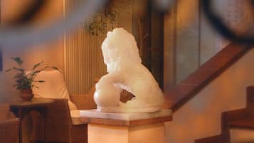 A white sculpture on a pedestal in a well-lit indoor space with wicker furniture and a staircase.