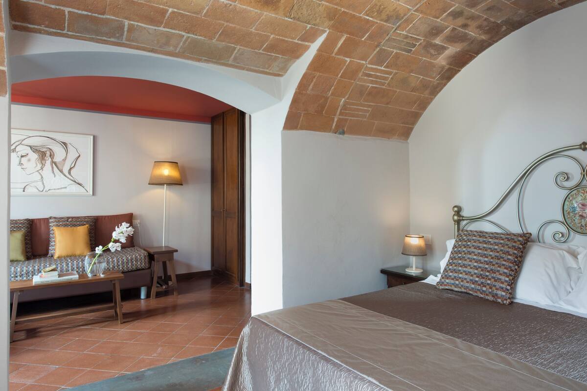 A bedroom with a bed, a nightstand, a lamp, a sofa, and a painting on the wall.