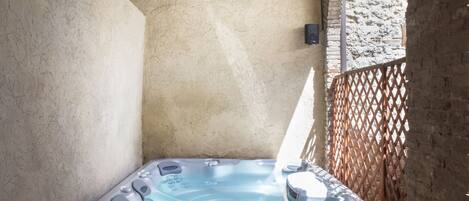 Un bain à remous installé dans une petite alcôve étroite et ensoleillée, avec un plancher en bois et un mur en briques.
