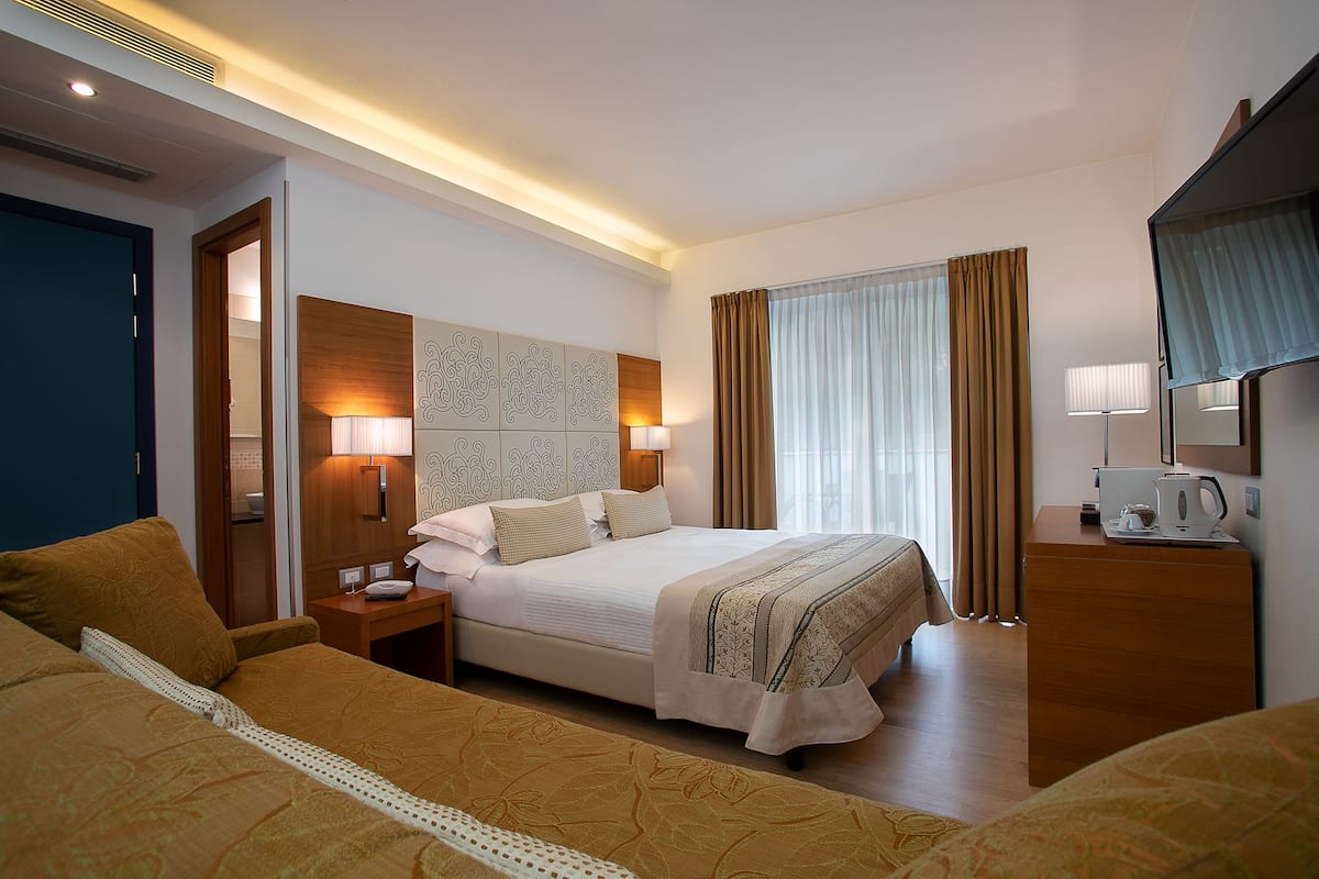 Une chambre d’hôtel avec un grand lit, des tables de chevet, un bureau, une lampe et une fenêtre avec des rideaux.