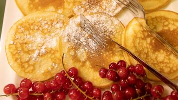 Ein Teller Pfannkuchen mit Puderzucker und einer Gabel, dazu eine Traube roter Trauben.