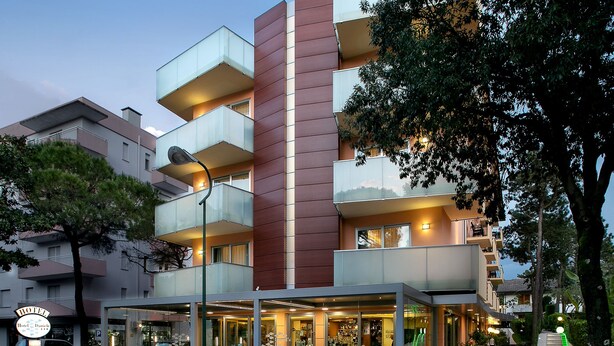 Un hotel moderno con fachada de vidrio, zona de estar al aire libre y bar visible.