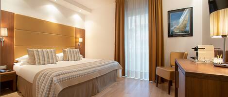 Habitación de hotel con una cama grande, un escritorio con lámpara, una silla y una ventana con cortinas.