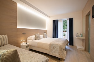 Una habitación de hotel moderna con una cama grande, una cama individual, una mesita de noche, un estante empotrado y un ventanal con cortinas.