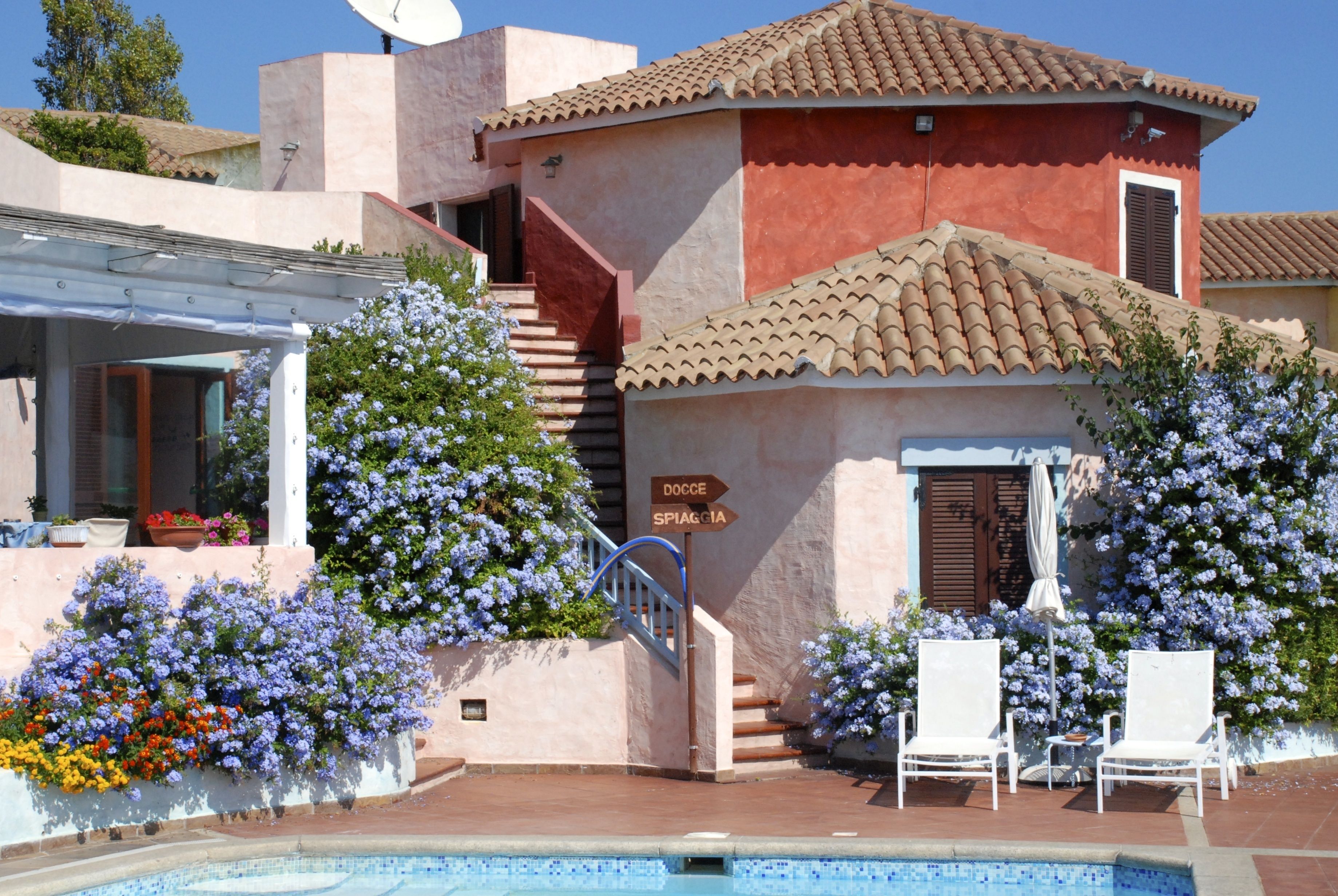 A building with a pool, white lounge chairs, and a sign indicating directions to 'DOCCE SPIAGGIA'.