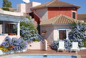 A building with a pool, white lounge chairs, and a sign indicating directions to 'DOCCE SPIAGGIA'.
