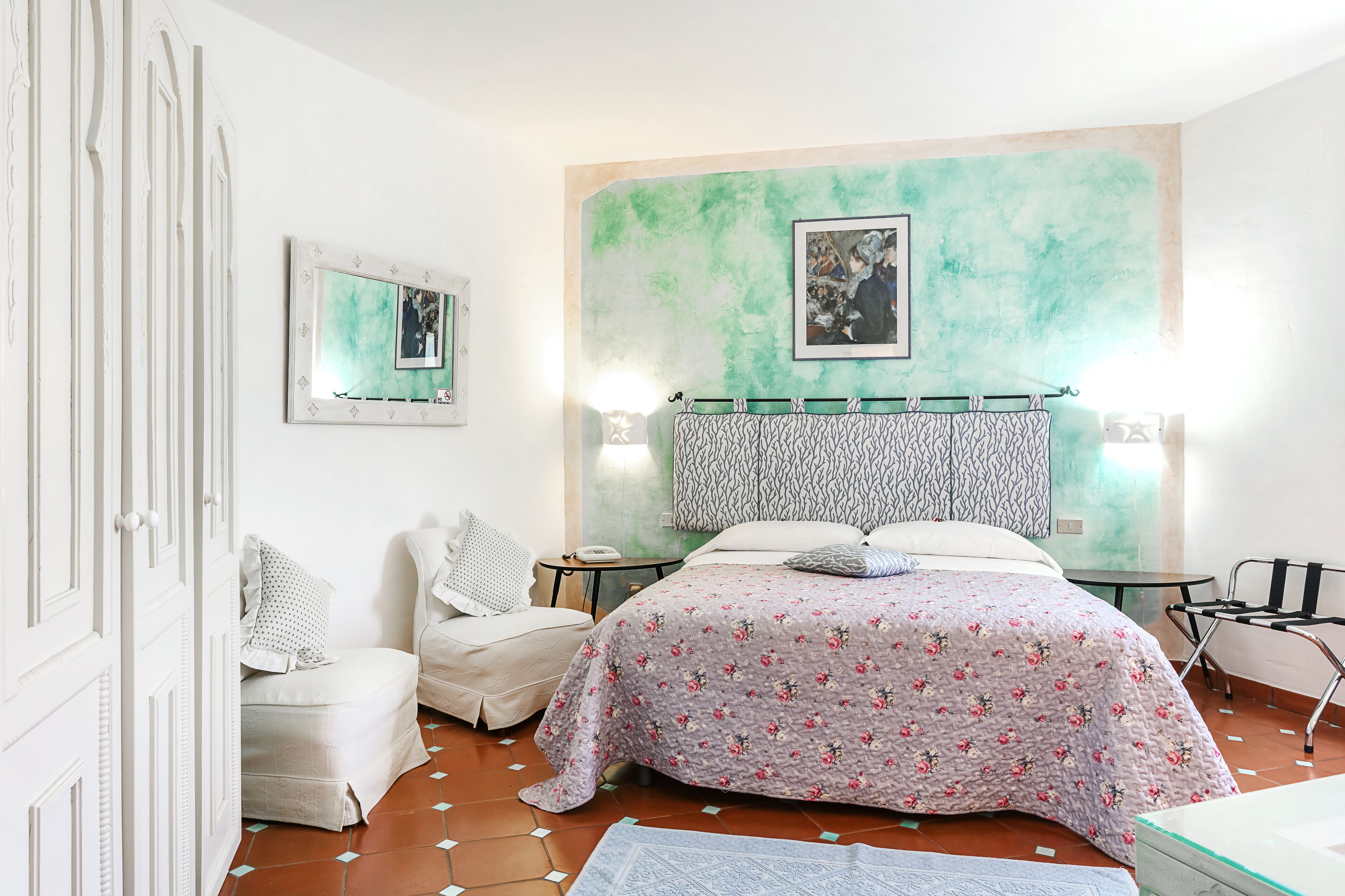 A bedroom with a bed, a chair, a bedside table, and a wall with a painting.