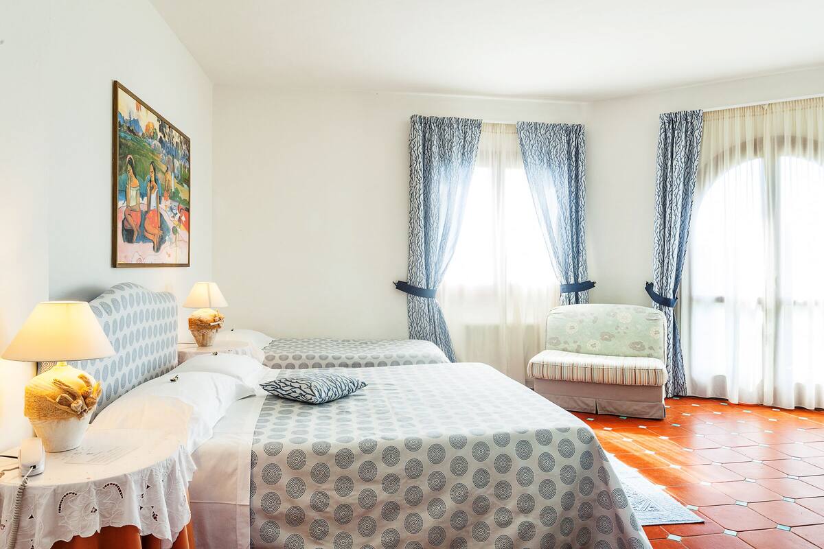 Habitación de hotel con dos camas, un sofá, un cuadro en la pared y una ventana con cortinas.