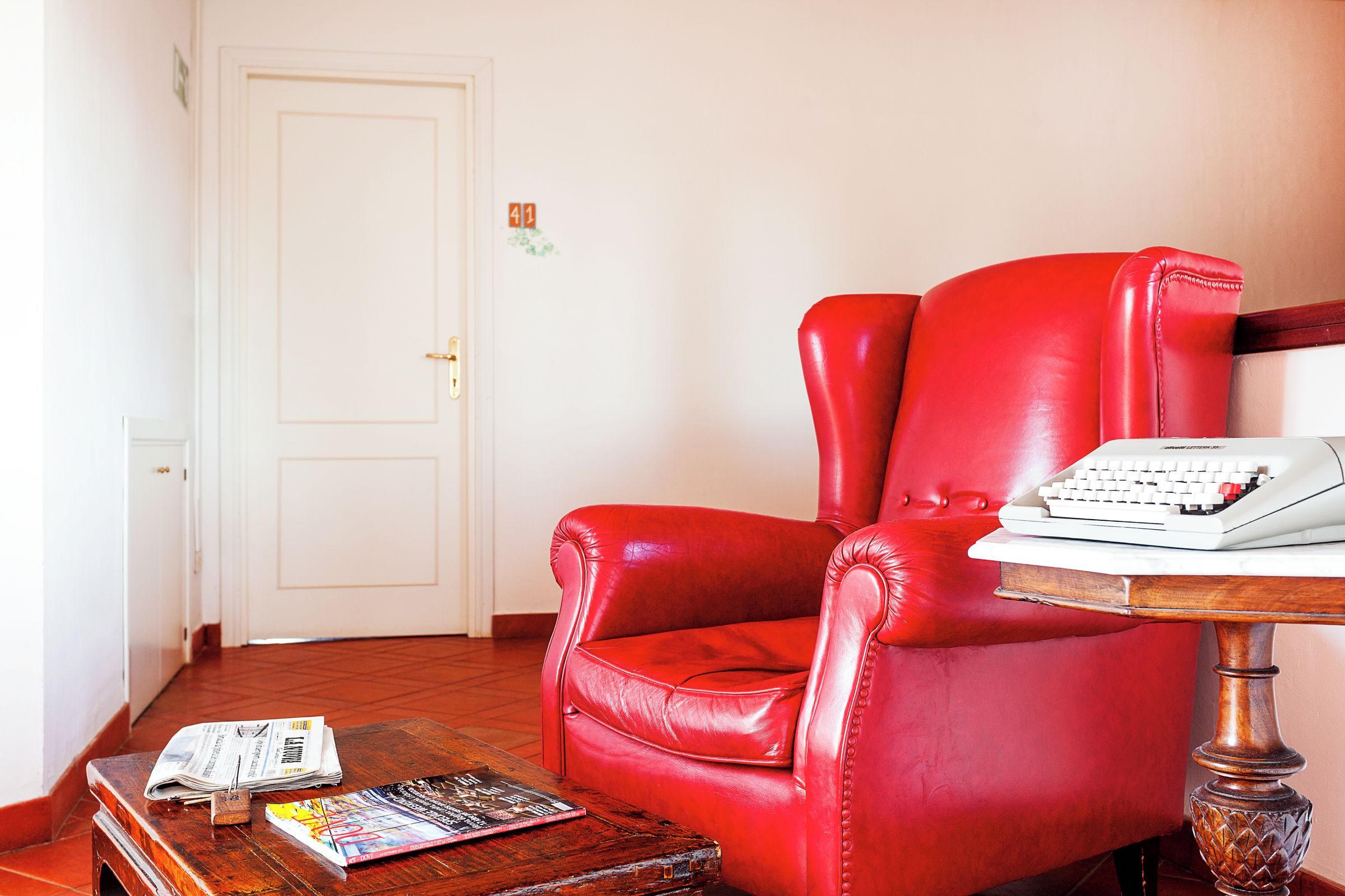 Un sillón rojo de cuero con un teclado blanco y un libro sobre una mesa de madera.