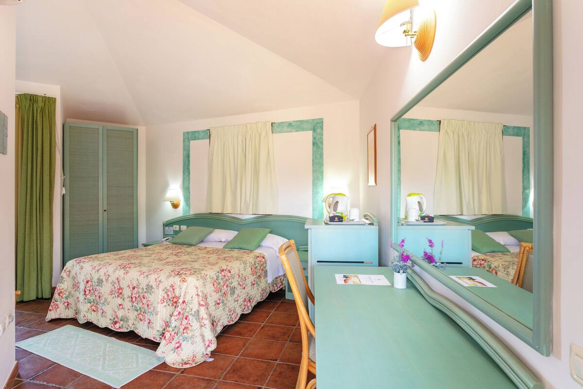 Un dormitorio con cama, mesita de noche, espejo y una silla verde.