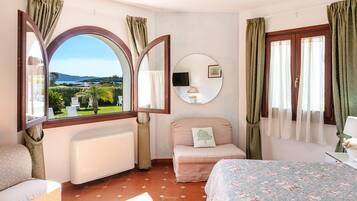 Un dormitorio con una ventana grande, una cama, una mesita de noche, una silla y una pequeña mesa con una lámpara.