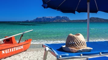 Een privéstrand, wit zand, ligstoelen aan het strand, parasols