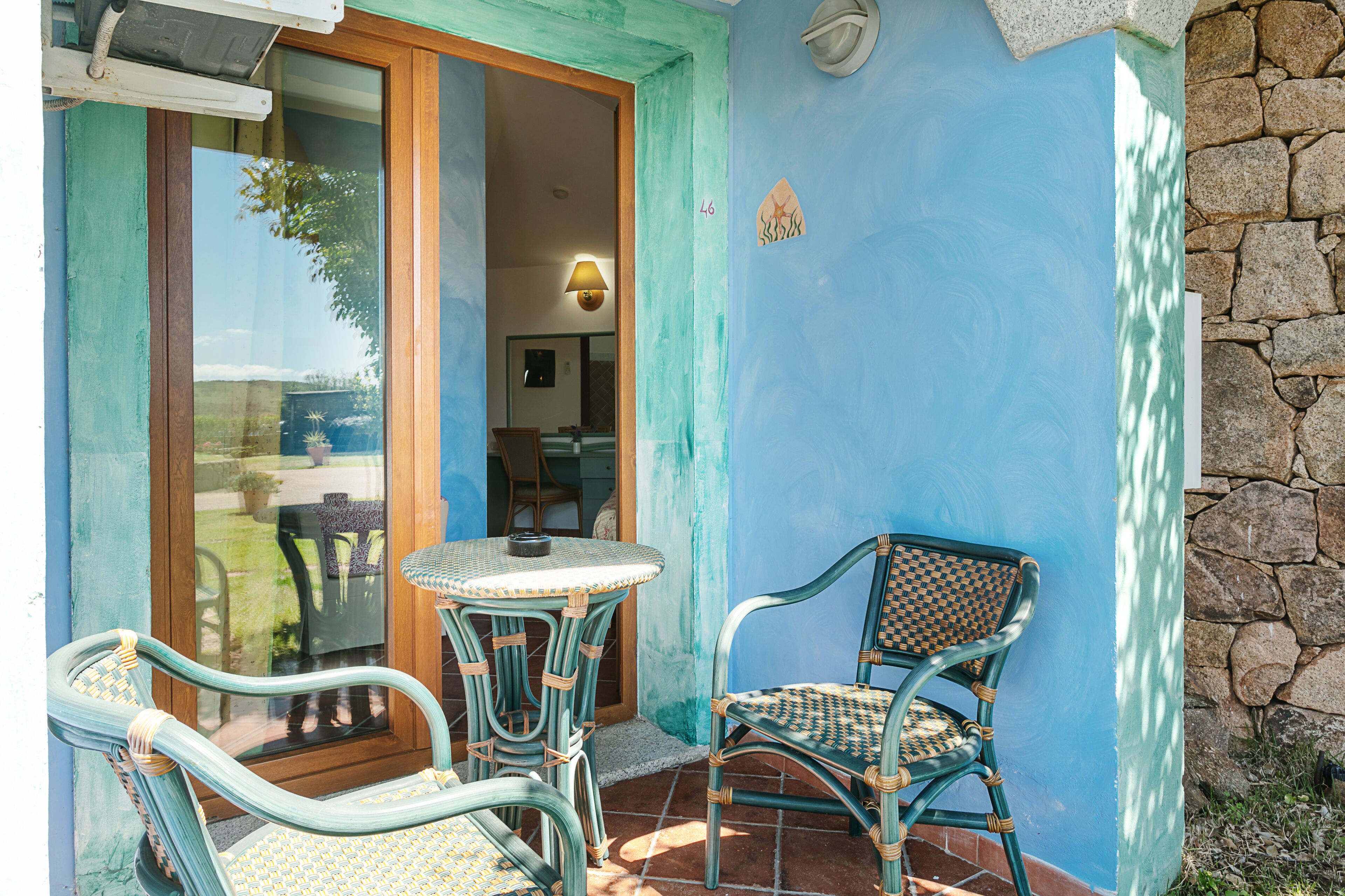 Un patio con mobiliario de mimbre, una mesa y un muro de piedra.