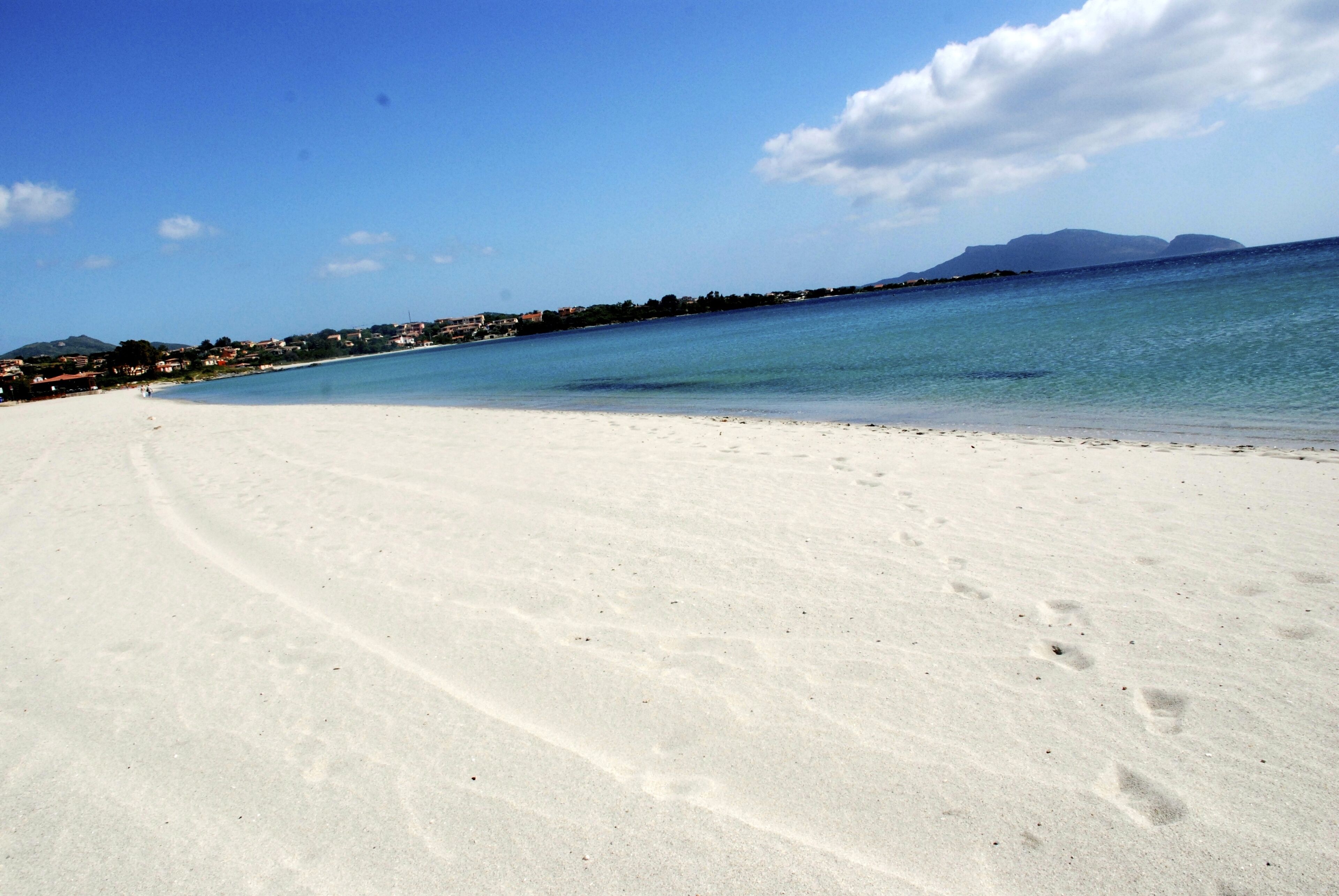 A wide sandy beach with clear blue water and distant mountains.