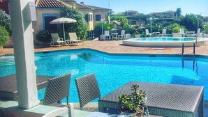Un área de comedor junto a la piscina, con una mesa preparada para dos, con vistas a una piscina y un jardín ajardinado.