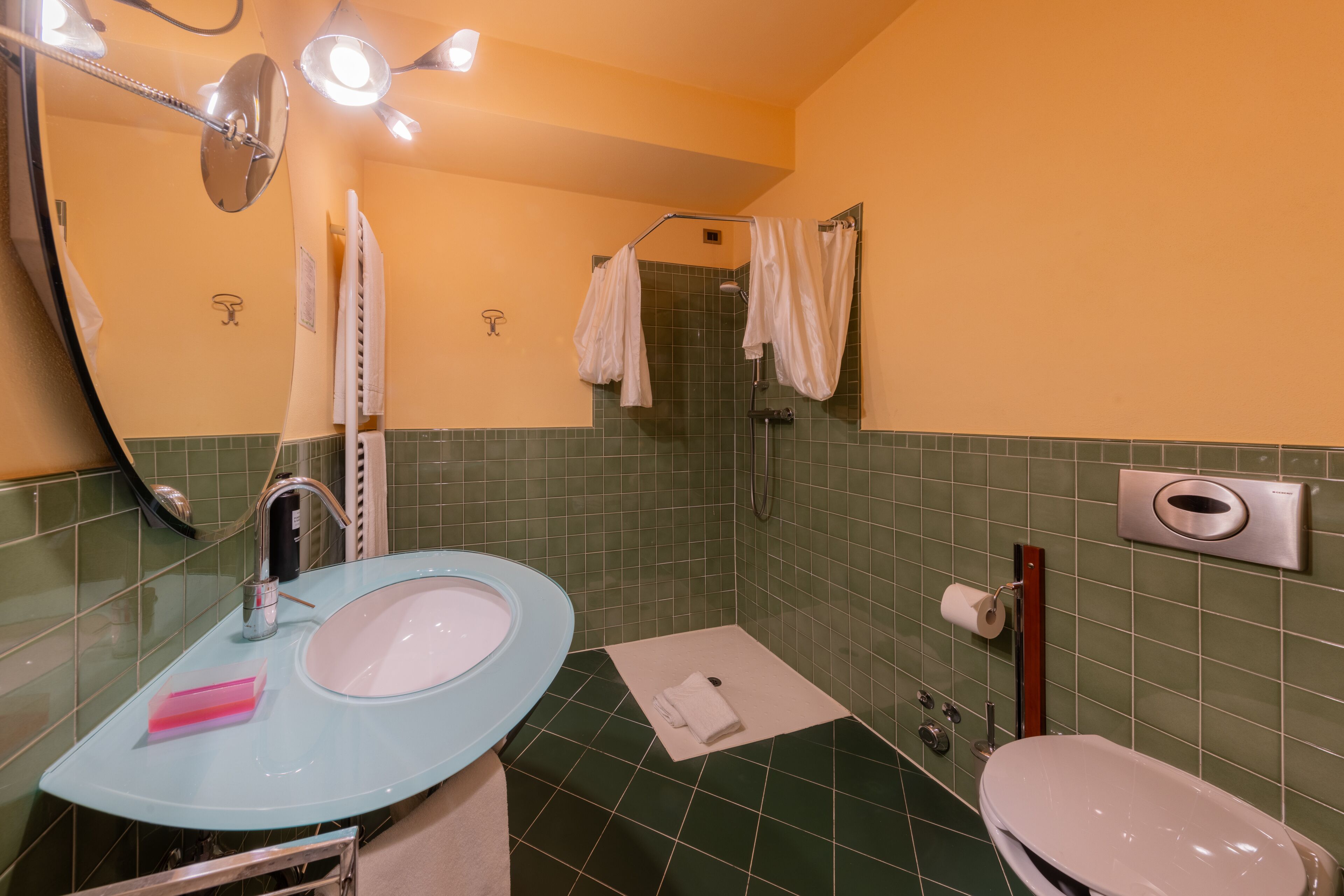 Et badeværelse med vask i glas, toilet, brusebad og et spejl.