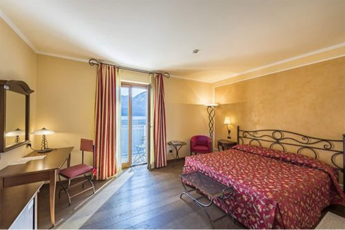 Una habitación de hotel con cama, escritorio, silla, una mesita y ventana con cortinas.
