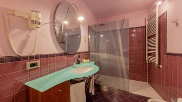 Un baño con pared de azulejos rosa y rojos, un lavamanos con encimera verde, un espejo, un secador de pelo y una zona de ducha.