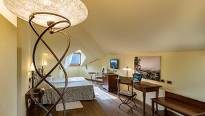 A cozy attic bedroom with a sloped ceiling, a bed with a patterned bedspread, a desk with a laptop, a chair, and a large floor lamp. - La Darsena Boutique Hotel & Restaurant (Tremezzina)