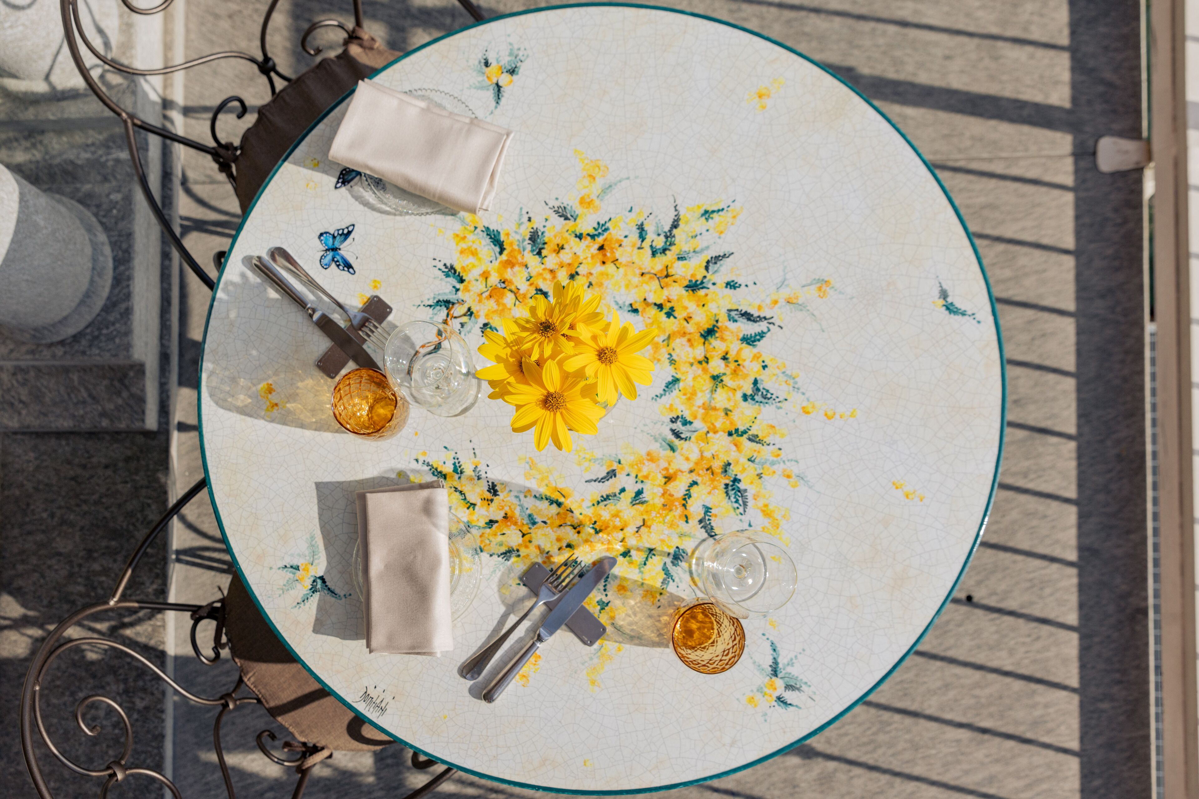 Ein runder Tisch mit einer blumigen Tischdecke, einer Vase mit gelben Blumen und einem Glas Wasser.