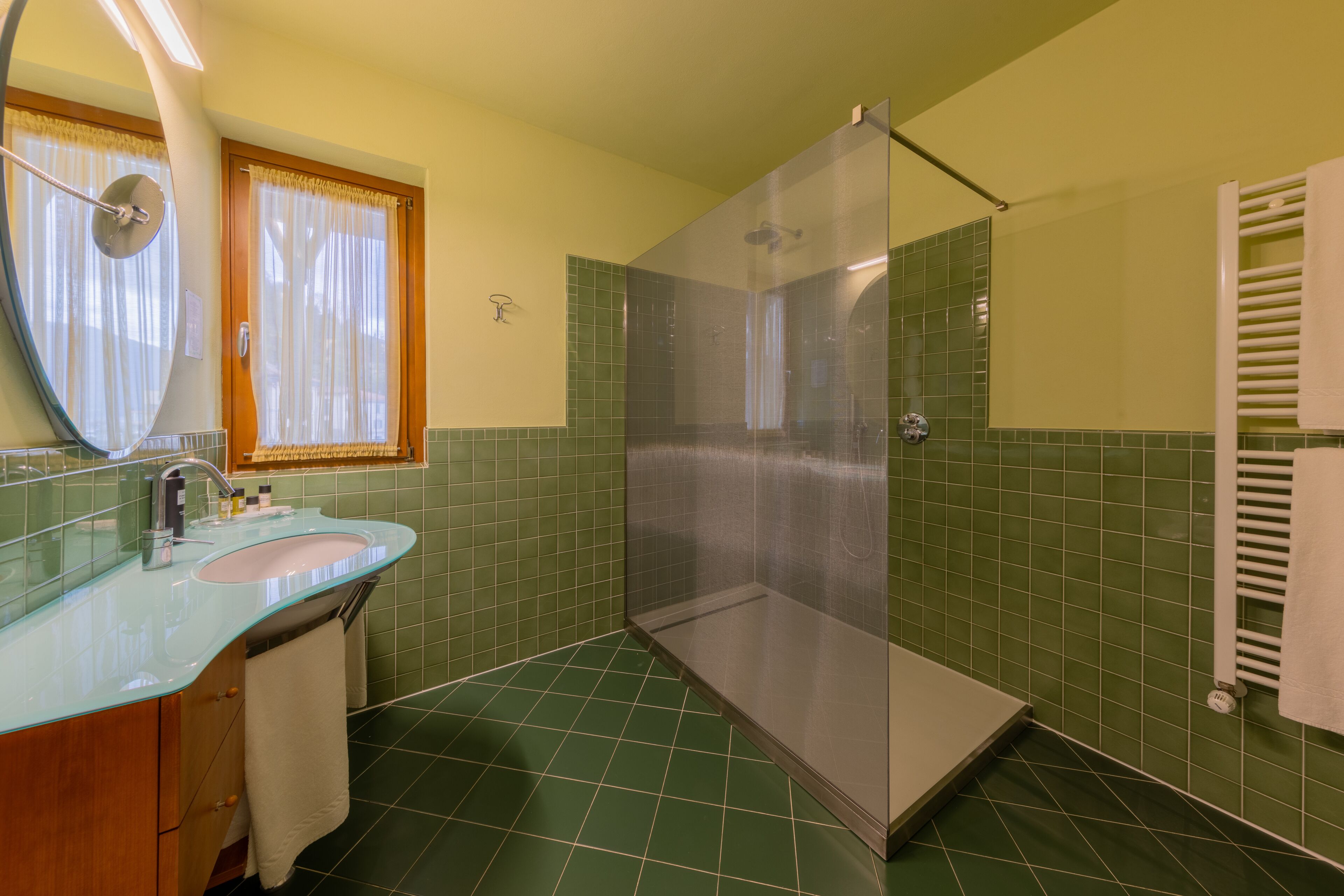 A bathroom with a glass-enclosed shower, a sink with a mirror, and green tiled walls.