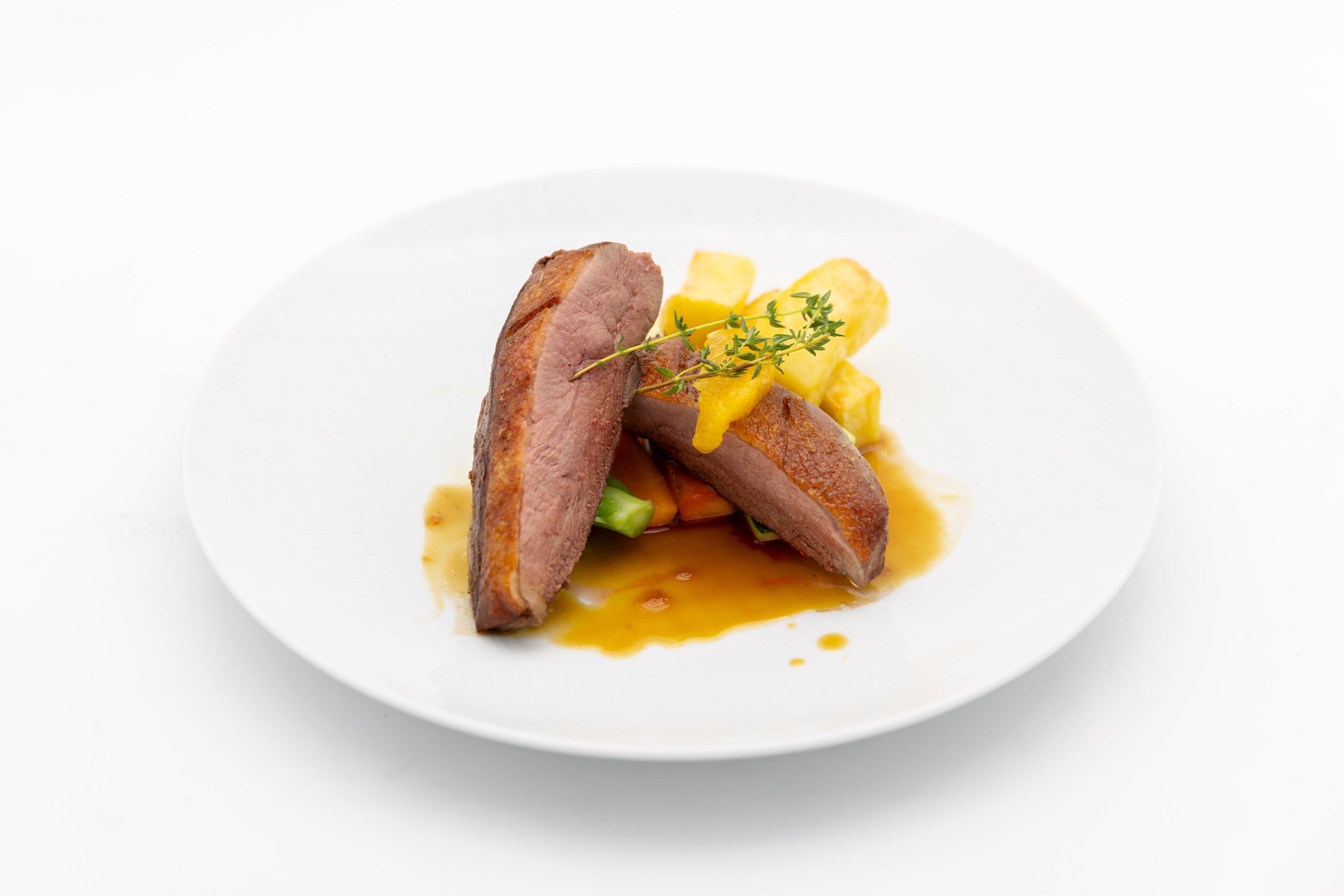 Une assiette contenant du canard, des pommes de terre et une garniture.