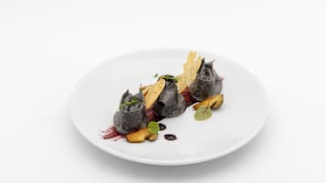 Un plato blanco con un alimento de color oscuro, posiblemente un postre, acompañado de algunos adornos y algunas porciones de algo que parece comida frita.