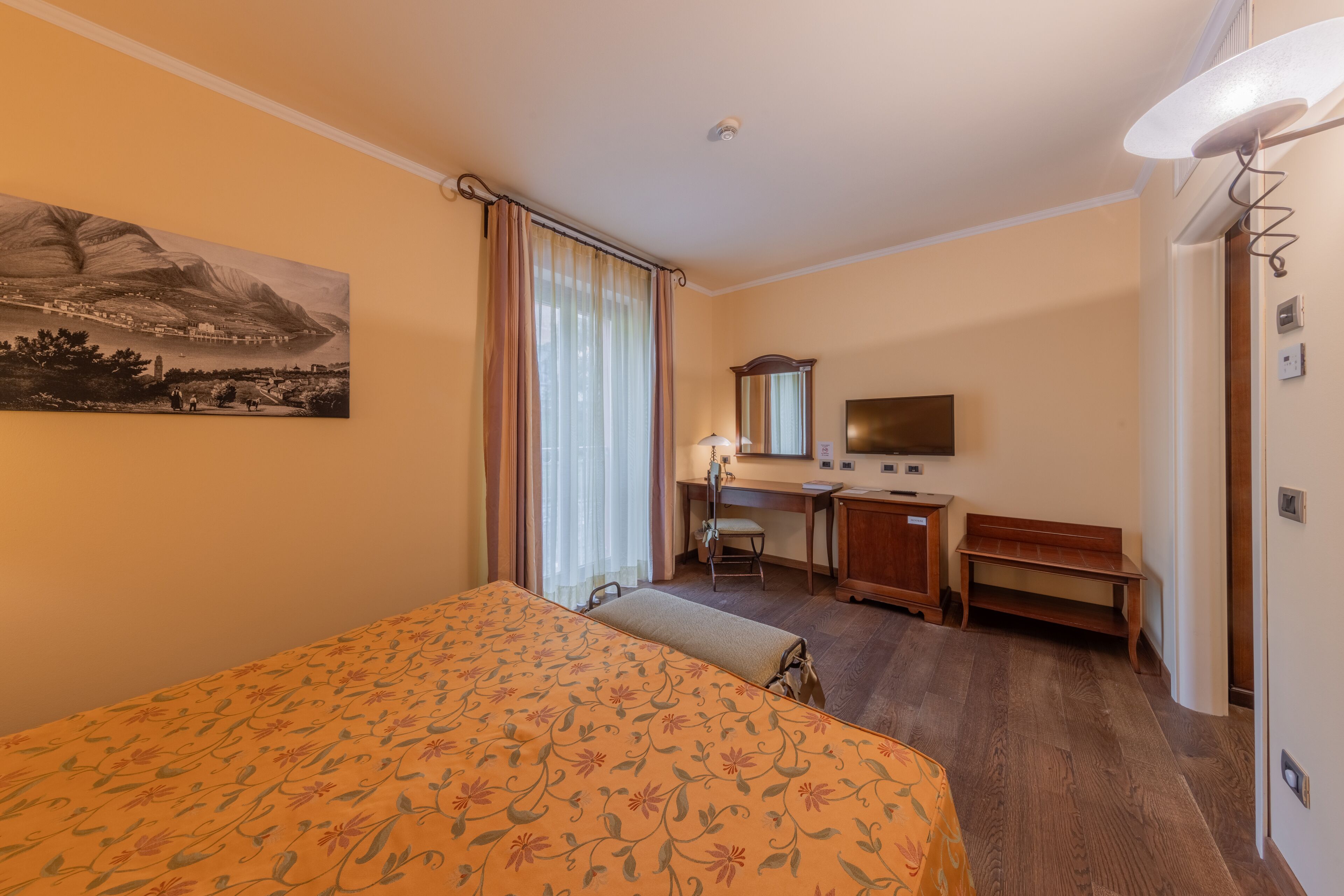 Habitación de hotel con cama, escritorio, silla y una ventana grande con cortinas.
