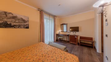 Habitación de hotel con cama, escritorio, silla y una ventana grande con cortinas.