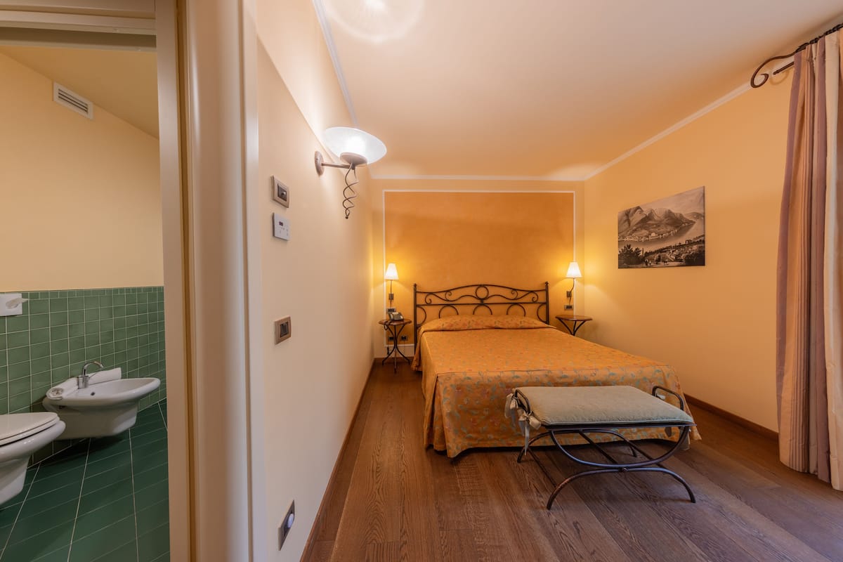 Un dormitorio con cama, lámparas de noche, un cuadro en la pared y un baño con lavabo e inodoro.