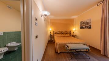 A bedroom with a bed, bedside lamps, a wall-mounted painting, and a bathroom with a sink and toilet.