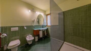 A bathroom with a toilet, bidet, sink, and a shower area.