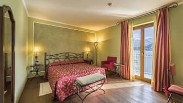 A bedroom with a bed, a chair, a table, and a view of mountains through the window.