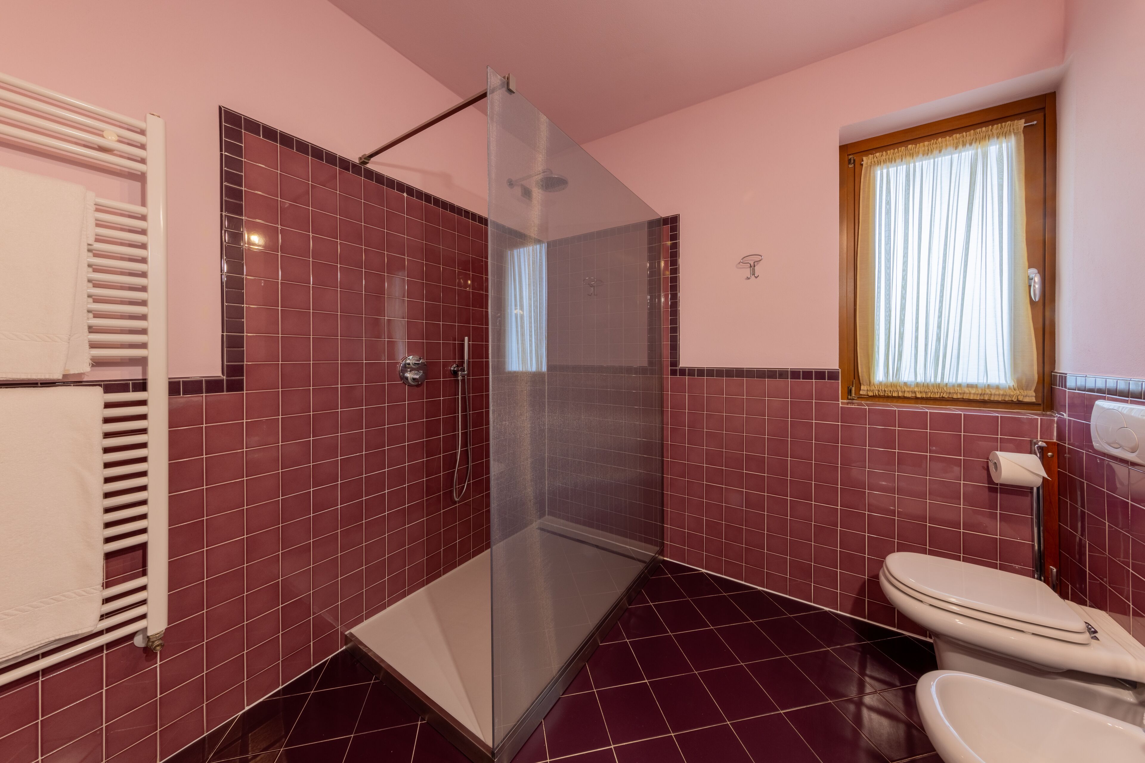 Une salle de bain avec une douche à parois de verre, des toilettes et une fenêtre avec des rideaux.