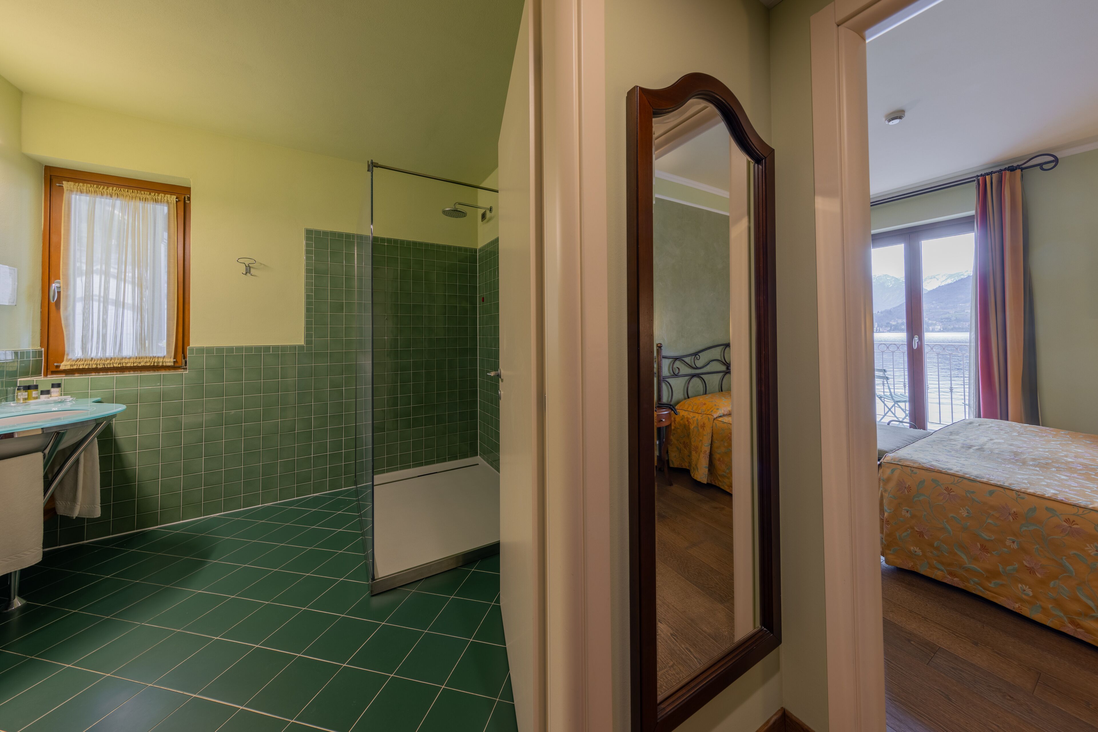 Un baño con baldosas verdes, ducha, lavamanos y espejo.