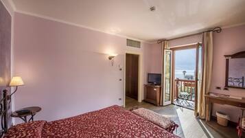 Habitación de hotel con cama, escritorio, televisión y balcón con vistas.