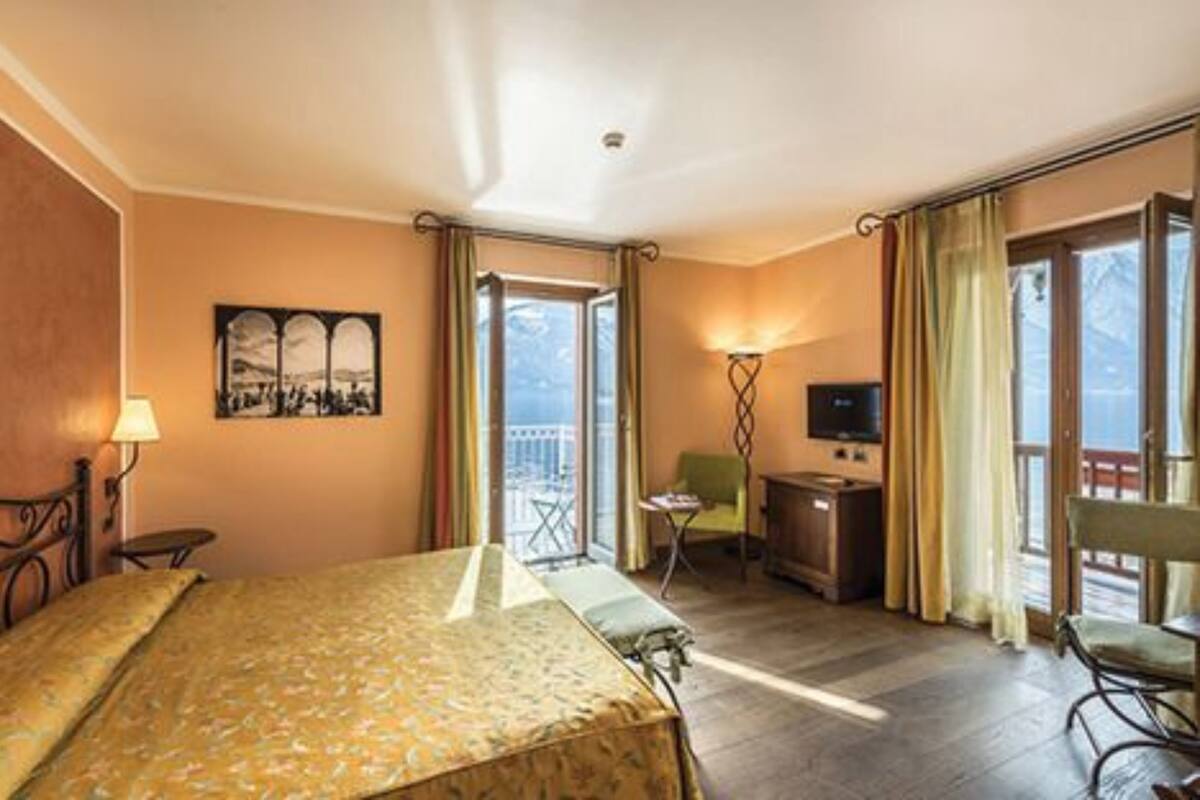 Habitación de hotel con cama, escritorio, silla, televisor y balcón con vistas.
