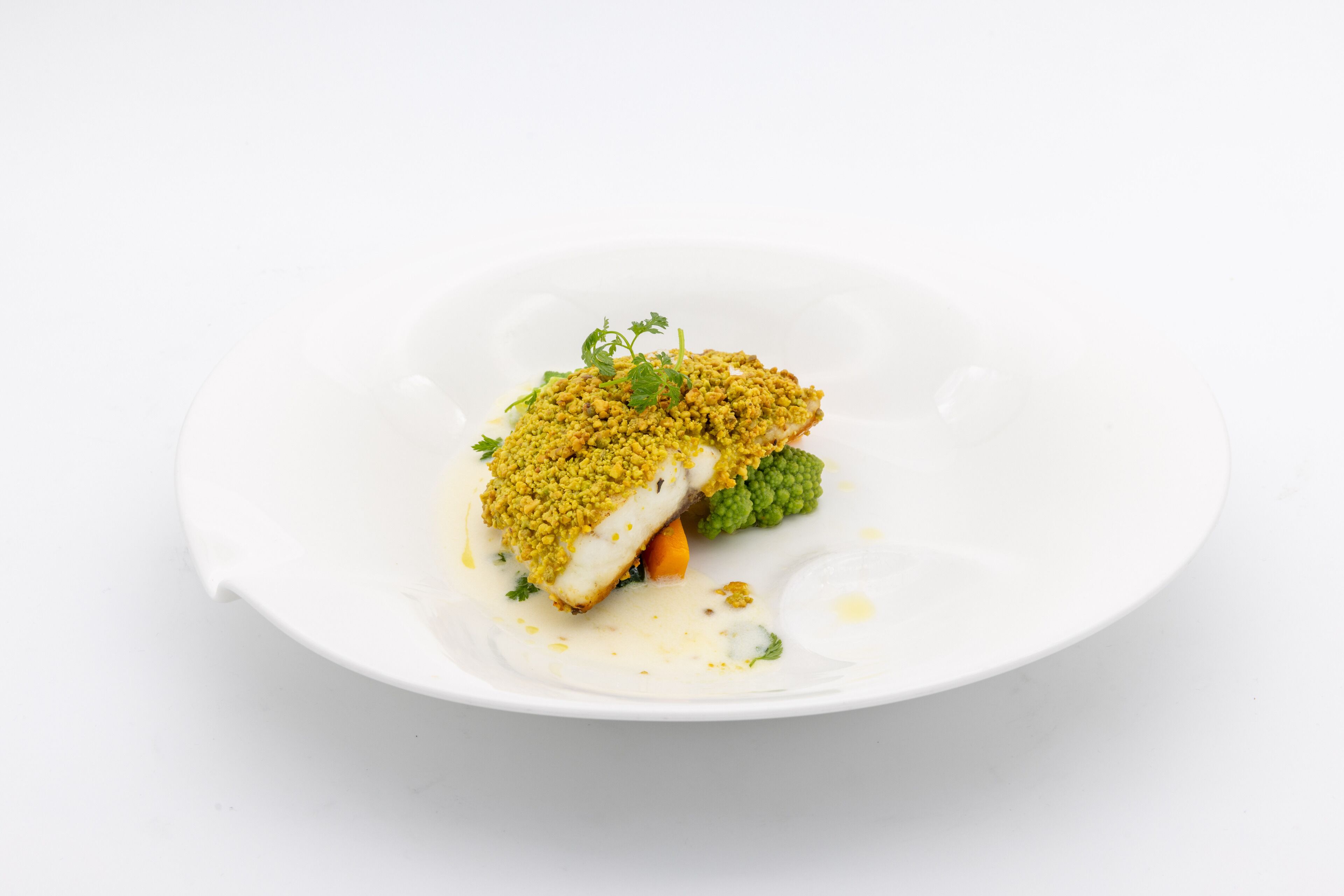 A white plate with a piece of fish topped with a yellow crumbly substance, accompanied by a green vegetable and a dollop of sauce.