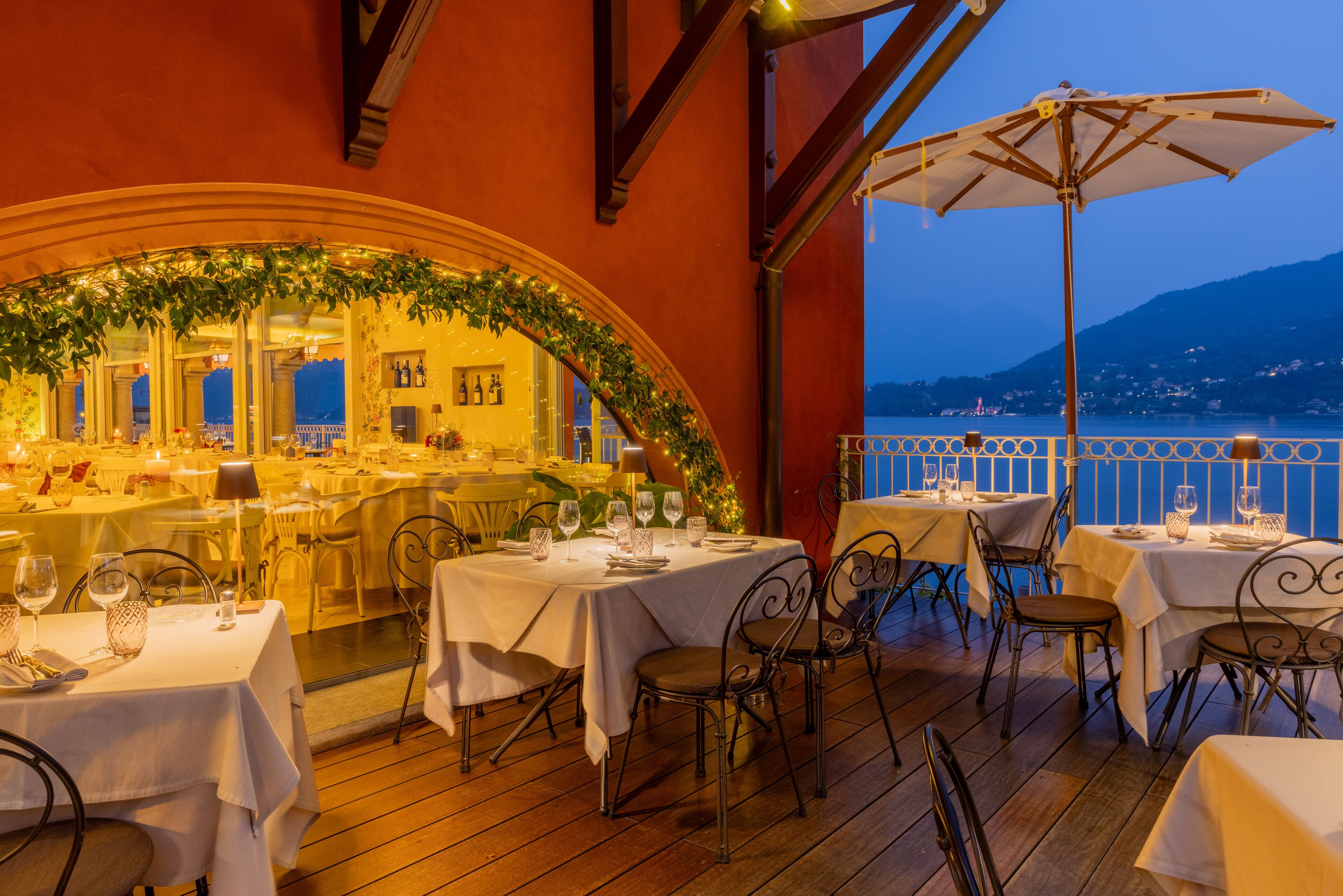 Un área de comedor al aire libre con mesas dispuestas para dos, con manteles blancos y sillas de metal.