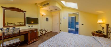 A hotel room with a bed, a desk, a chair, a mirror, and a bathroom visible through an open door.