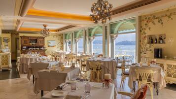 Un restaurante con varias mesas, elegantes candelabros y vistas al mar.