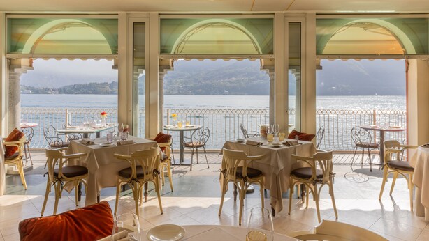 A restaurant with tables and chairs arranged for dining, large windows offering a view of a body of water and a mountainous landscape. - La Darsena Boutique Hotel & Restaurant (Tremezzina)