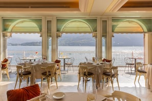 A restaurant with tables and chairs arranged for dining, large windows offering a view of a body of water and a mountainous landscape. - La Darsena Boutique Hotel & Restaurant (Tremezzina)