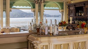 A bar area with a view of a lake, bottles of liquor, and a decorative bird on the wall. - La Darsena Boutique Hotel & Restaurant (Tremezzina)