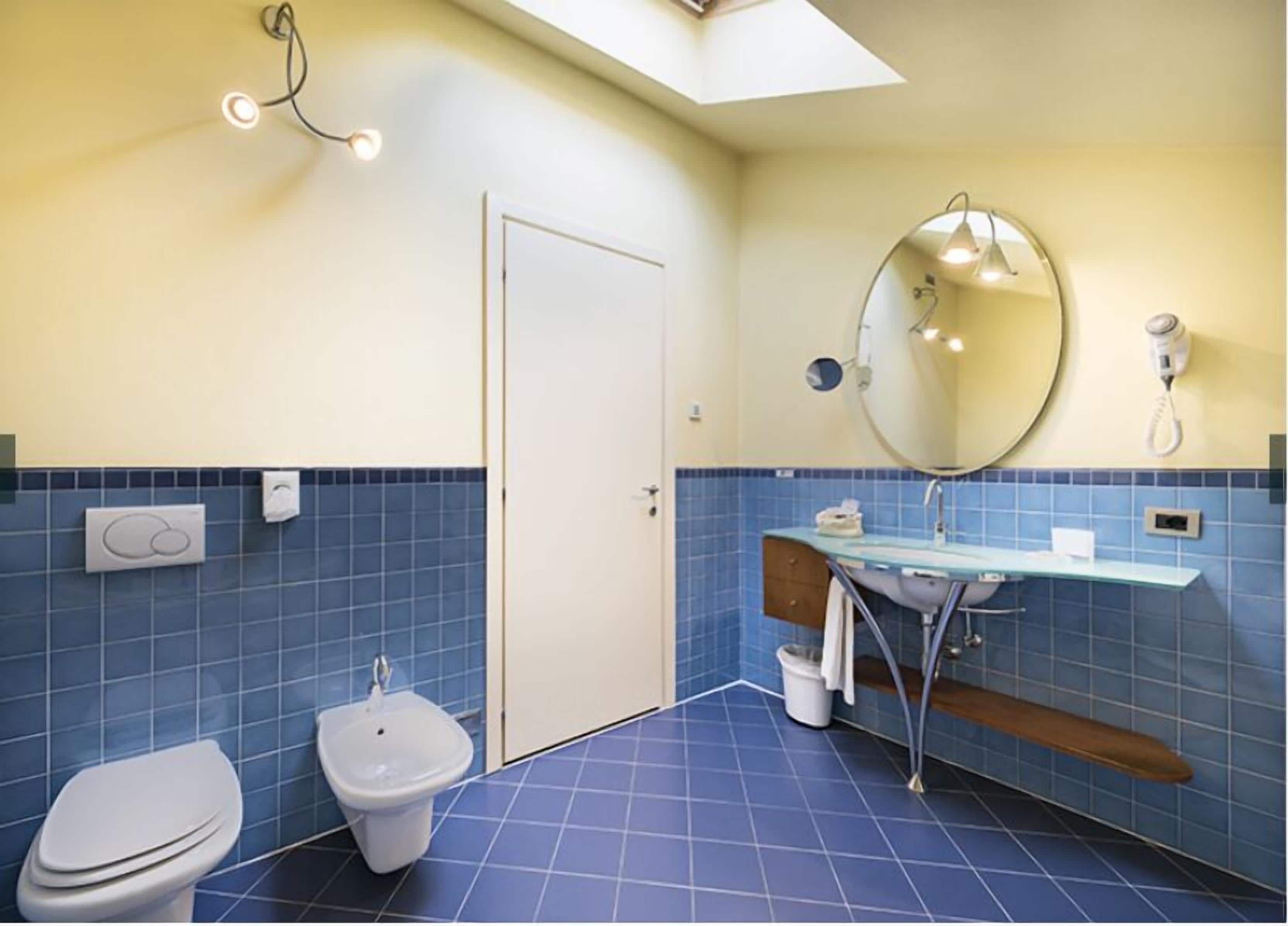 Un baño con inodoro, bidé, lavamanos, espejo y toallero.