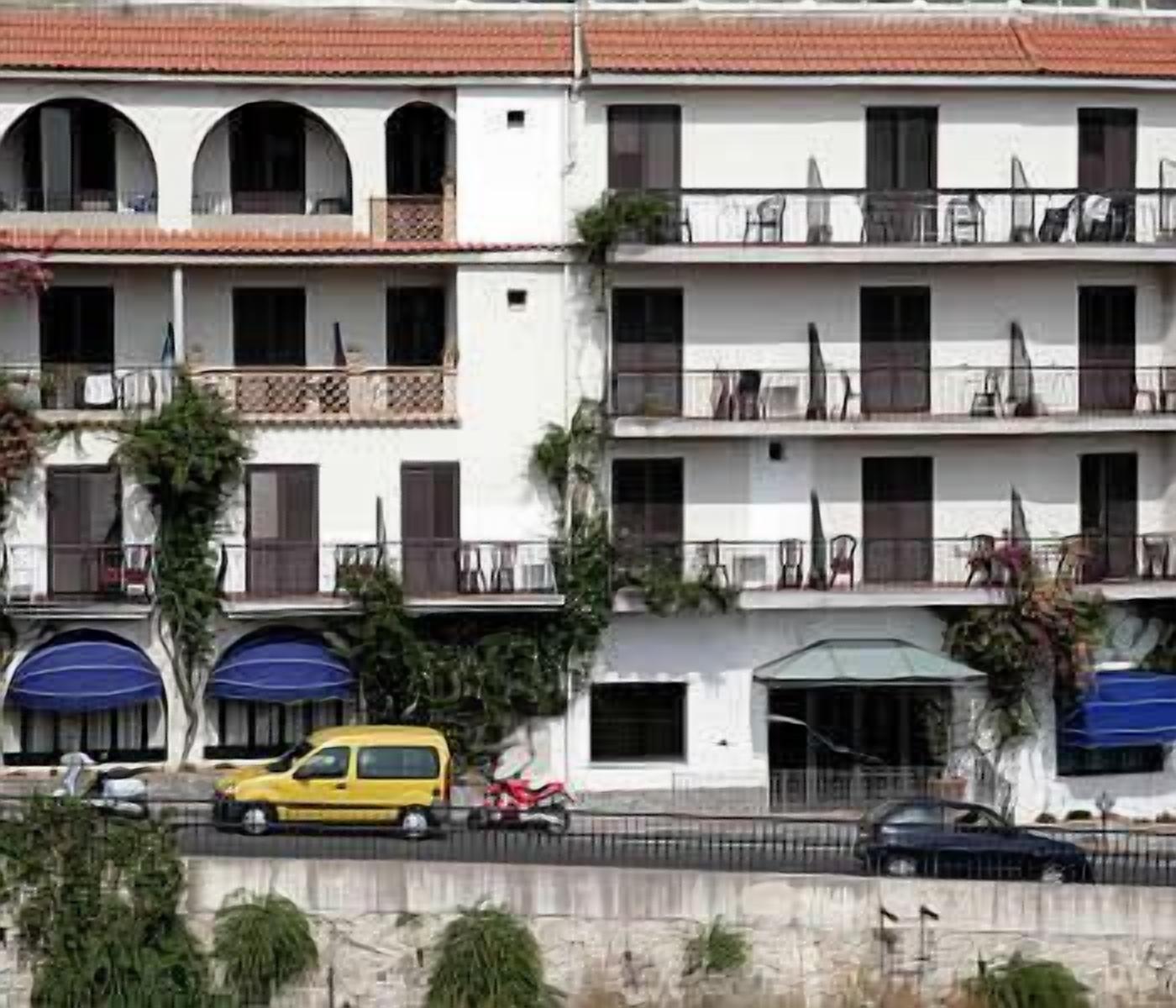 Un immeuble à plusieurs étages doté de balcons, un fourgon jaune garé devant, et une moto rouge.