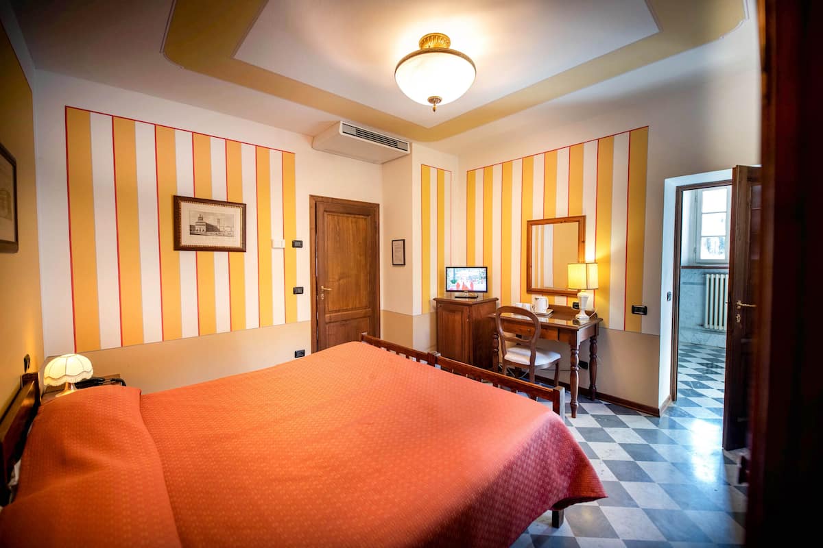 A hotel room with a bed, a desk with a computer, a chair, a lamp, and a picture on the wall.